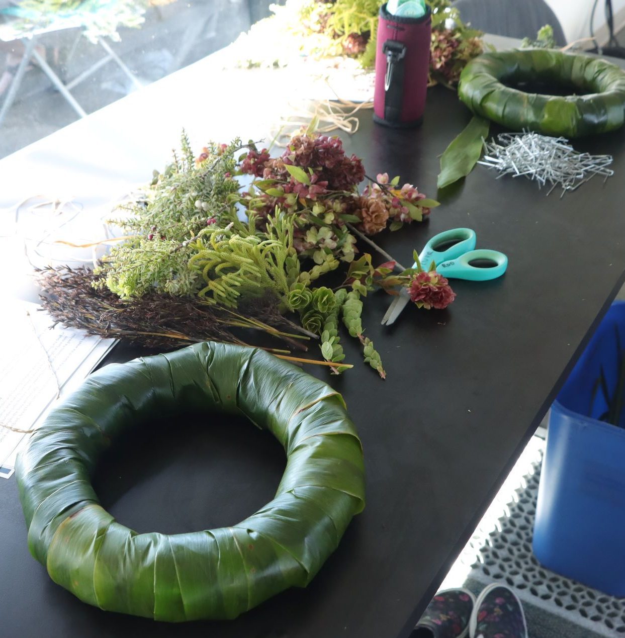 Wreath materials laid out on a brown table including the form, foliage, scissors, pins, etc.